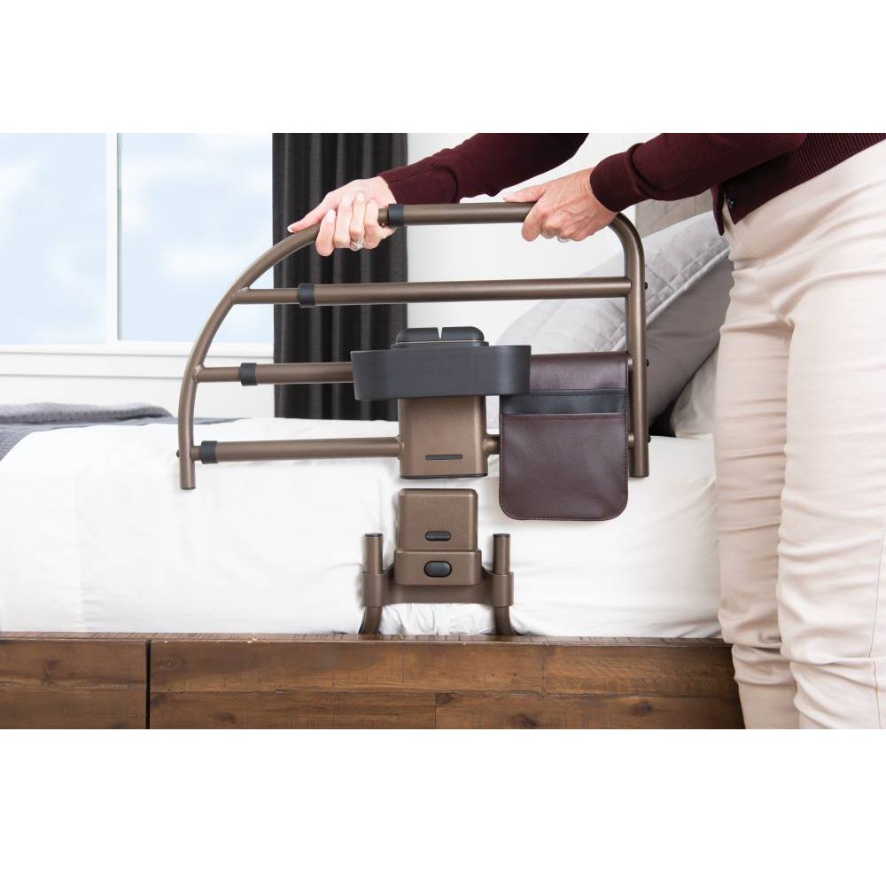 Braune Bett-Haltestange mit Halterungen und einer braunen Tasche, die an einem Bett befestigt ist.