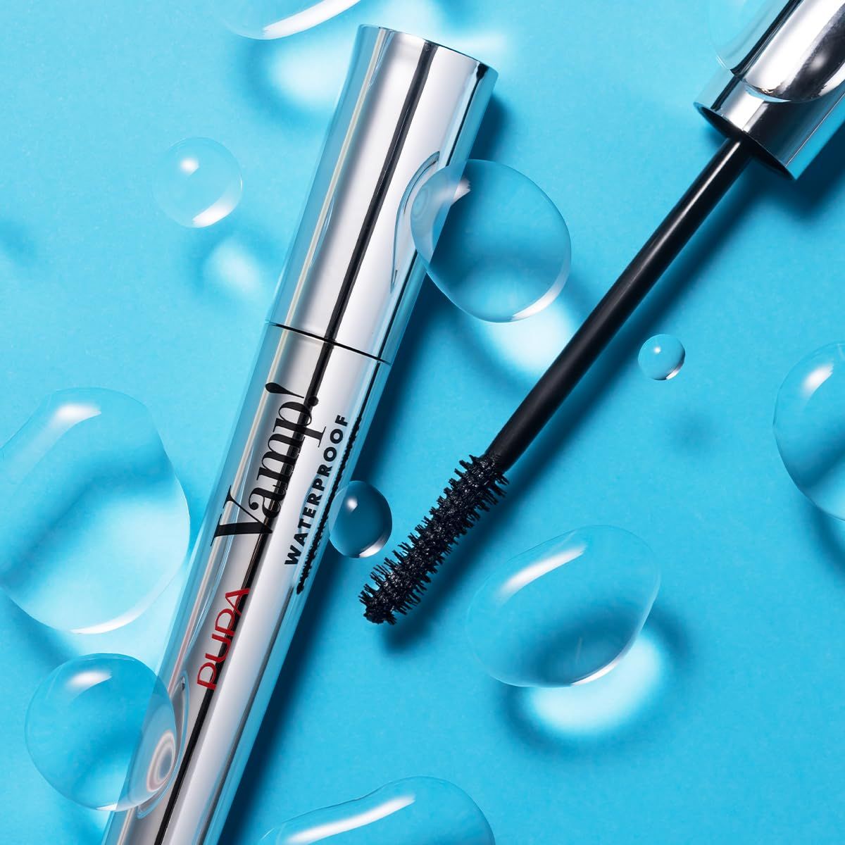 Mascara-Tube mit geöffneter Bürste. Silberne Tube, schwarze Bürste. Wasser auf blauem Hintergrund.