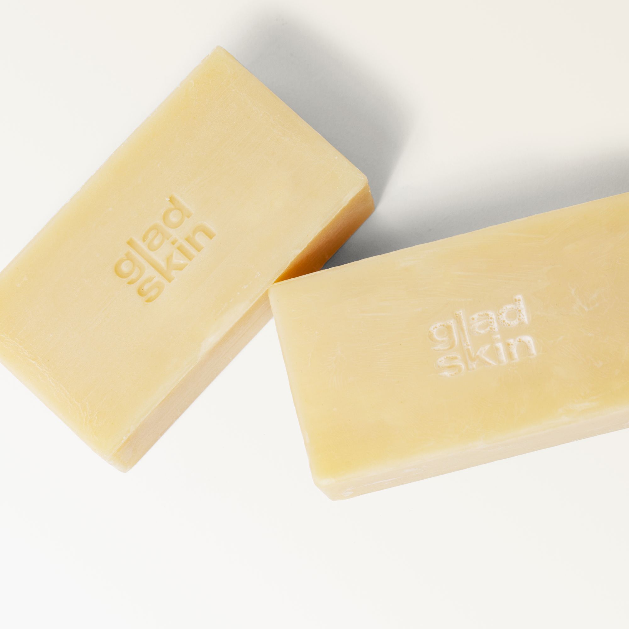 Zwei rechteckige Seifenstücke. Aufschrift: "gladskin". Helle, cremefarbene Seifenstücke auf weißem Hintergrund.
