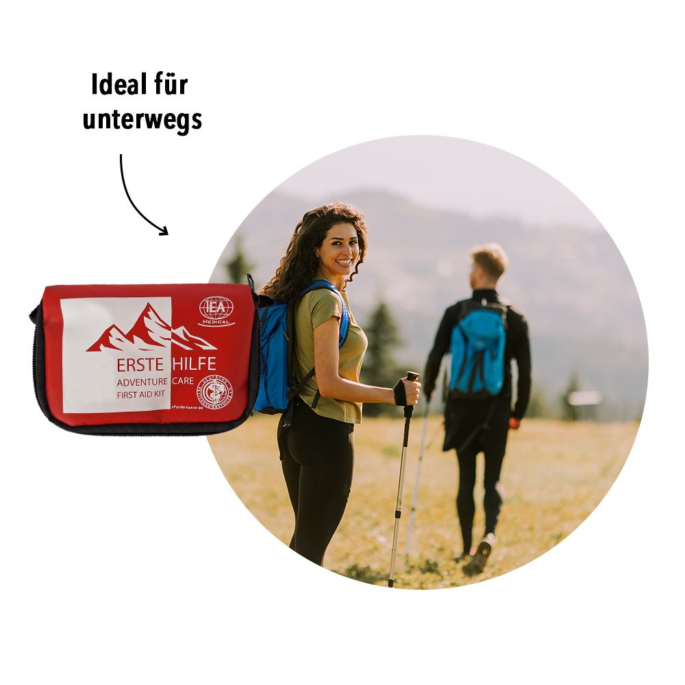Personen wandern mit Rucksäcken. Im Vordergrund: Rotes Erste-Hilfe-Set. Text: Ideal für unterwegs.