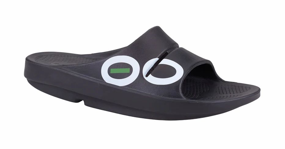 Schwarze Sport-Badesandale mit weißem Logo. Seitliche Ansicht. OOFOS-Schriftzug. Geformtes Fußbett. Riemen über dem Spann.