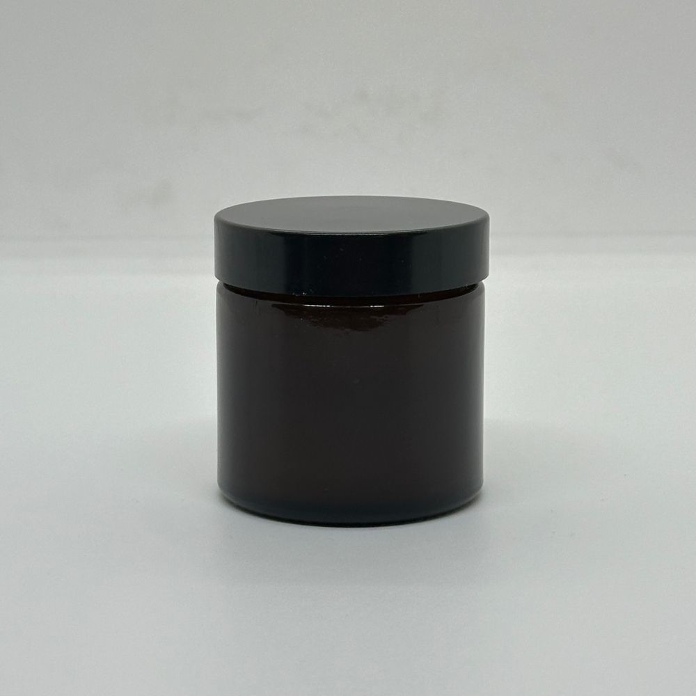 Braune Glasdose mit schwarzem Deckel. Zylindrische Form, auf hellem Hintergrund.