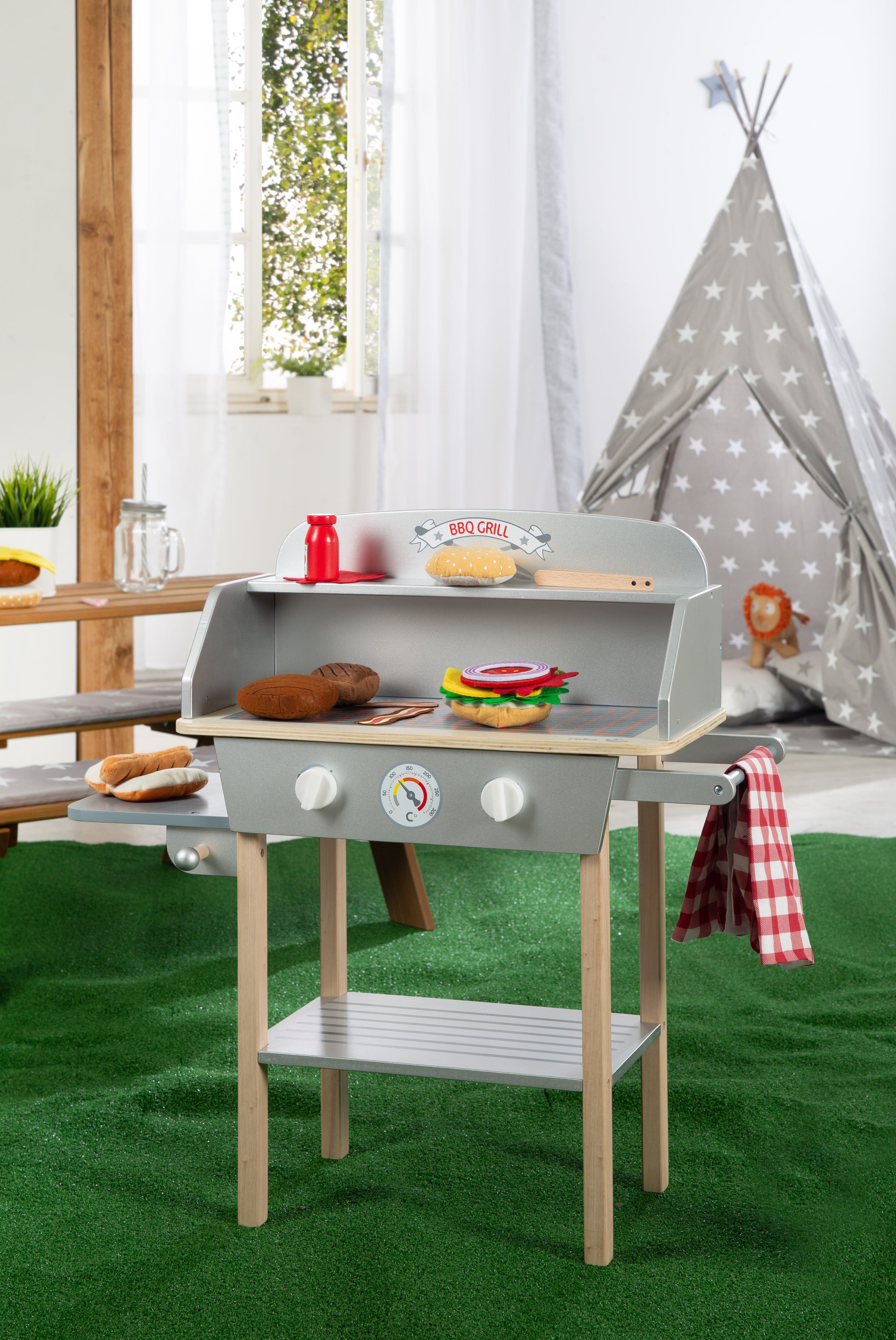 Spielzeug-BBQ-Grill mit Zubehör. Grauer Grill mit Holzbeinen, zwei Kochfeldern, Thermometer und Ablage. Aufschrift BBQ GRILL.