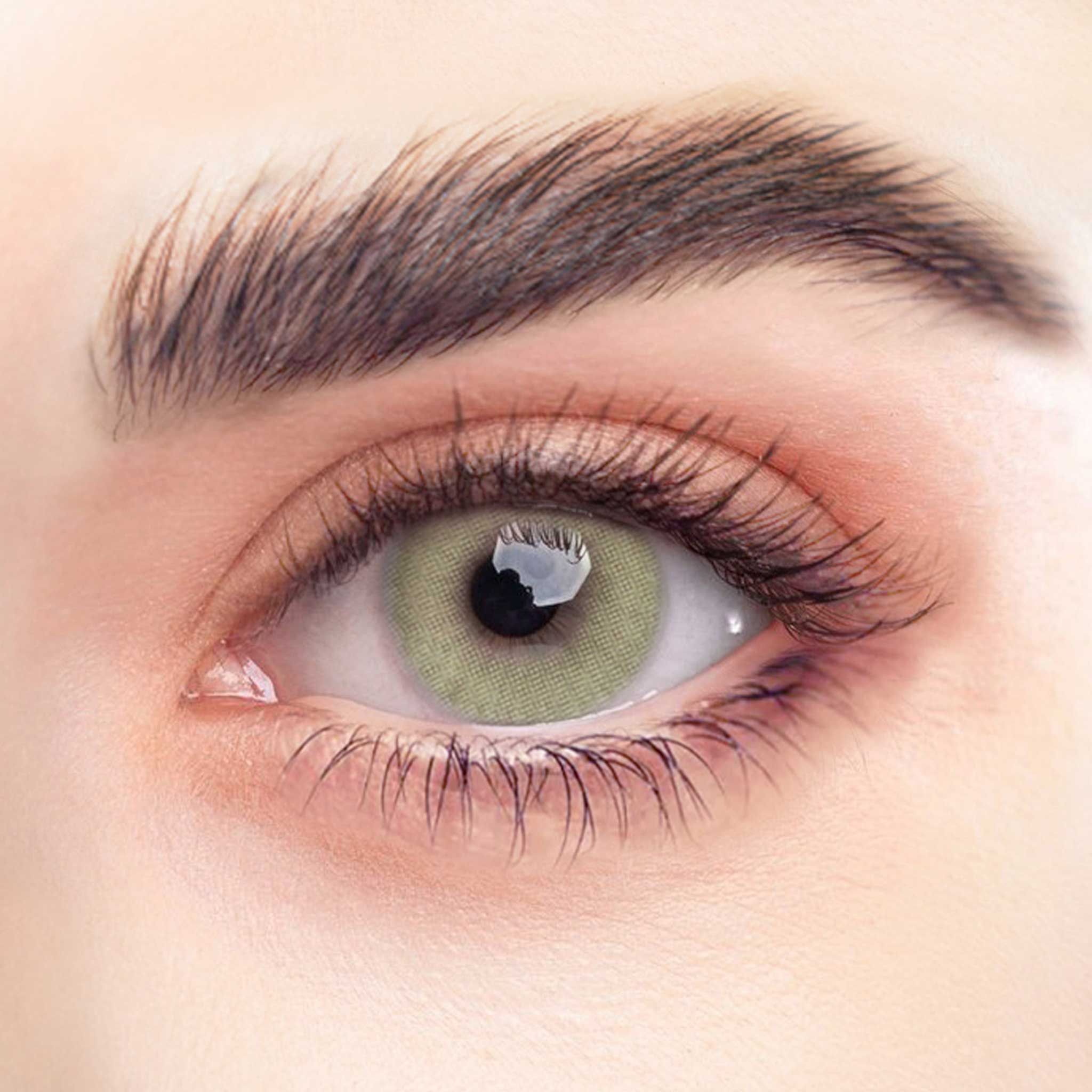 Nahaufnahme eines Auges mit grüner Kontaktlinse. Die Iris ist grün. Wimpern und Augenbrauen sind deutlich sichtbar.