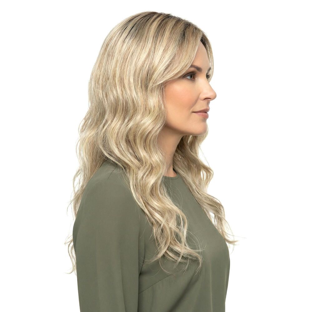 Blond gewellte Perücke mit Pony, Seitenansicht. Die Frau trägt ein grünes Oberteil. Hintergrund weiß.