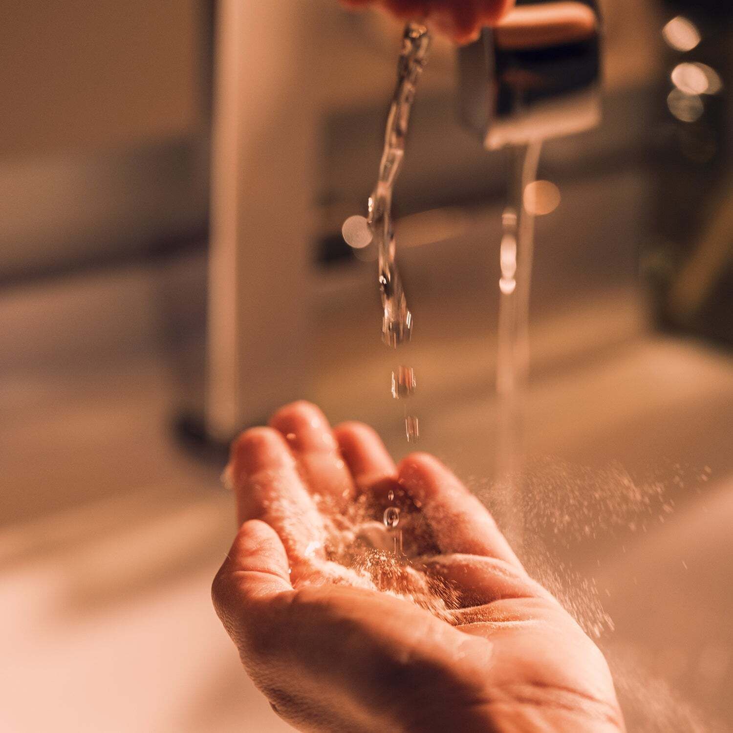 Hände unter fließendem Wasser. Hintergrund: Waschbecken und Wasserhahn.