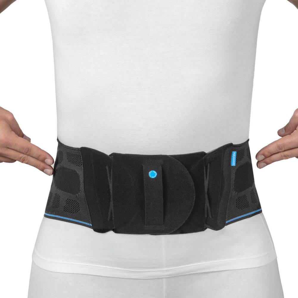 Person trägt eine schwarze Lumbalbandage. Bandage hat Klettverschlüsse und blaue Akzente. Person trägt weißes T-Shirt.
