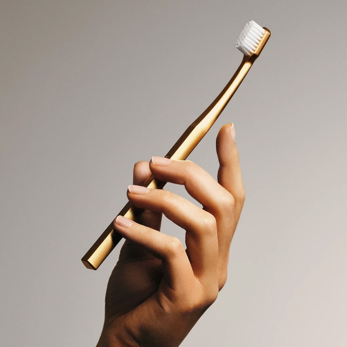 Hand hält eine goldene Zahnbürste. Der Griff ist schmal und rechteckig. Der Bürstenkopf ist klein.