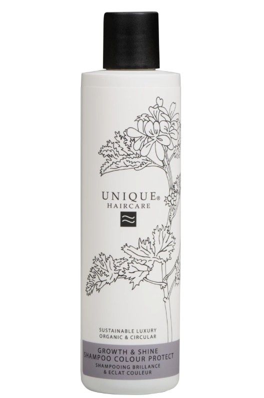 Flacon de shampooing blanc avec bouchon noir. Inscription: UNIQUE HAIRCARE, Growth & Shine Shampoo Colour Protect. Décor floral.