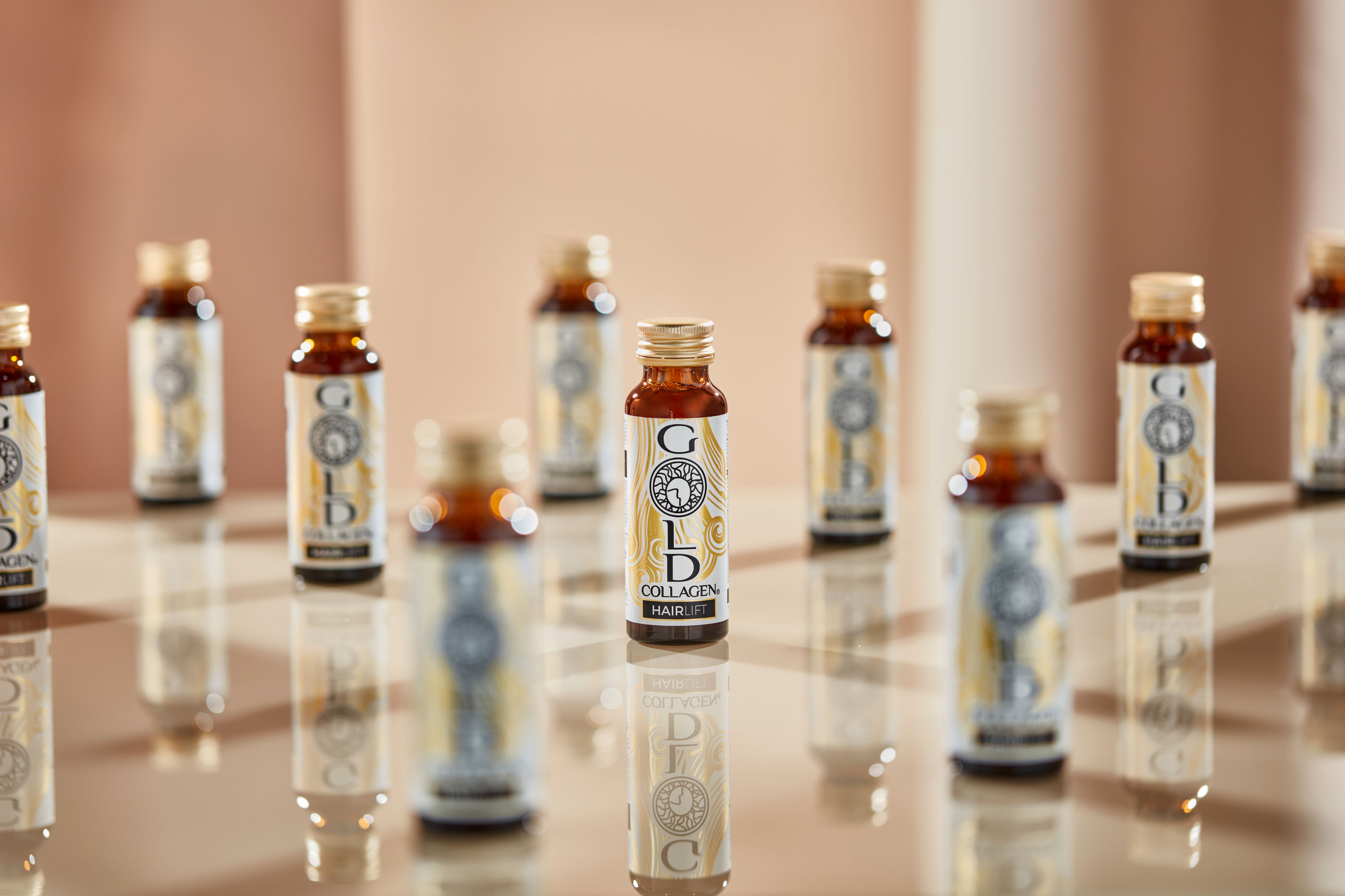 Mehrere braune Glasflaschen mit Gold Collagen Hairlift-Etikett. Auf einer glänzenden Oberfläche angeordnet.