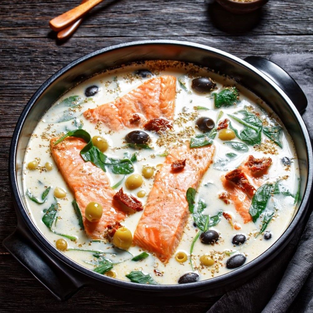 Lachs in cremiger Sauce mit Oliven und Spinat in einer Pfanne. Draufsicht.
