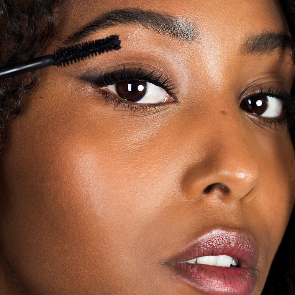 Nahaufnahme einer Frau, die Mascara aufträgt. Bürste am Auge. Dunkle Haut, dunkle Haare.