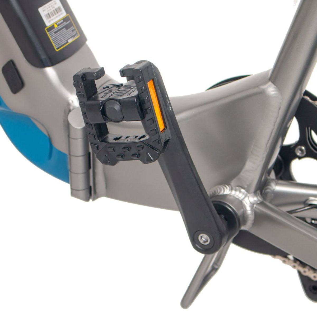 Nahaufnahme eines schwarzen Pedals mit orangefarbenem Reflektor. Teil eines grau-blauen E-Bikes.