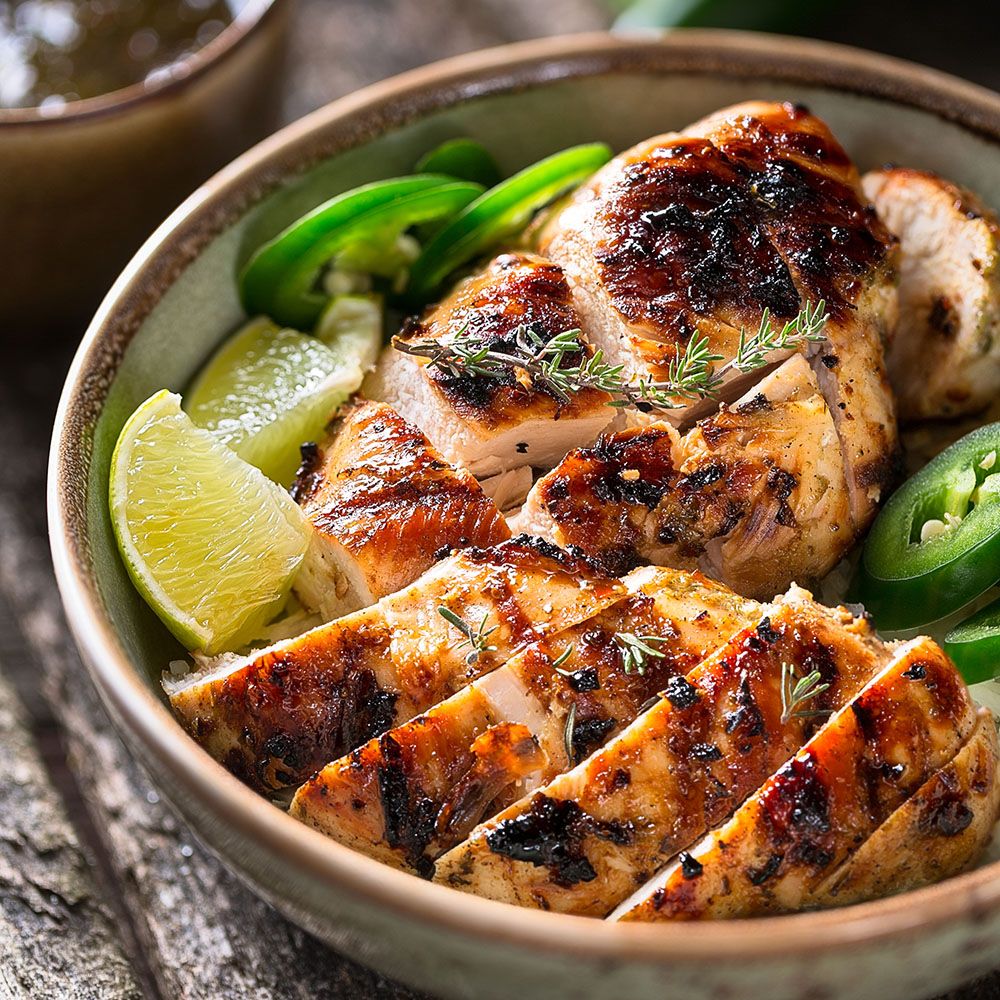 Gegrilltes Hähnchen in einer Schüssel. Scheiben, garniert mit Limetten, Jalapeños und Kräutern. Nahaufnahme.