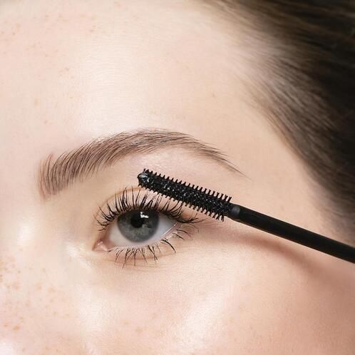 Auge mit Wimperntusche. Schwarze Mascara-Bürste wird auf die Wimpern aufgetragen.