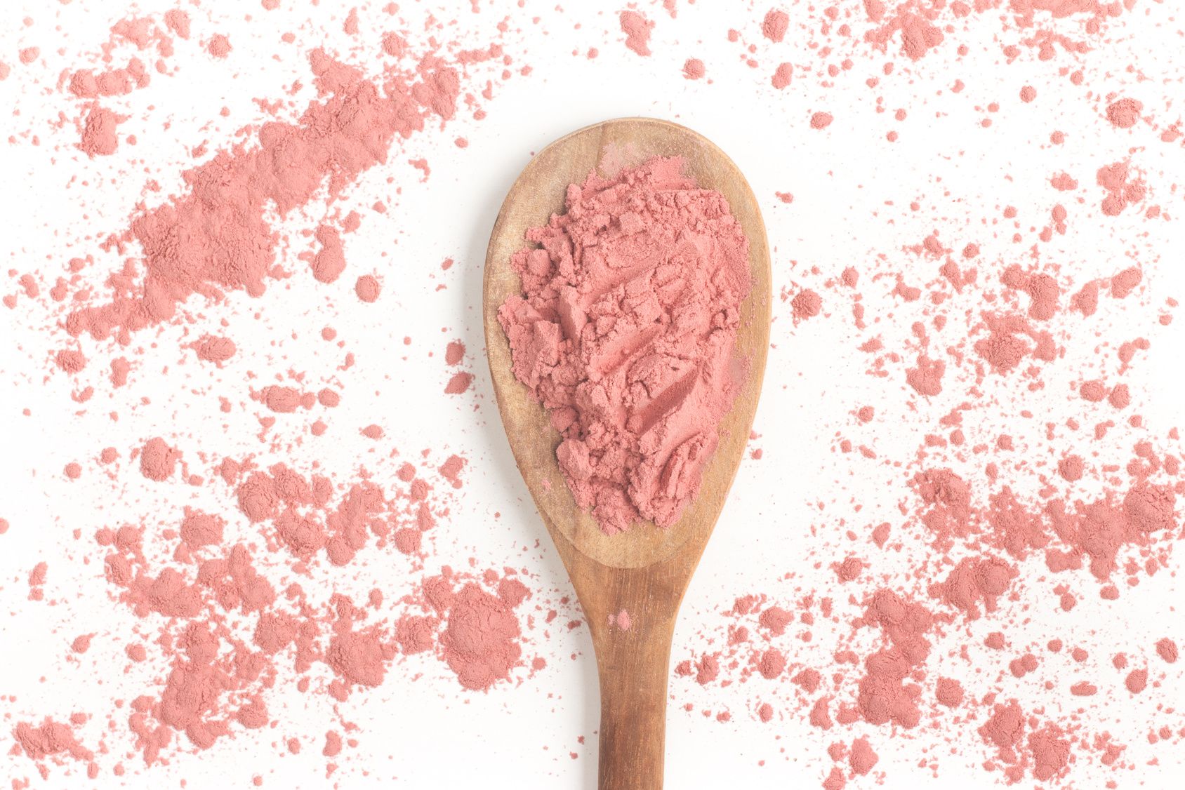 Holzlöffel mit rosa Pulver. Pulver verstreut auf weißem Hintergrund.