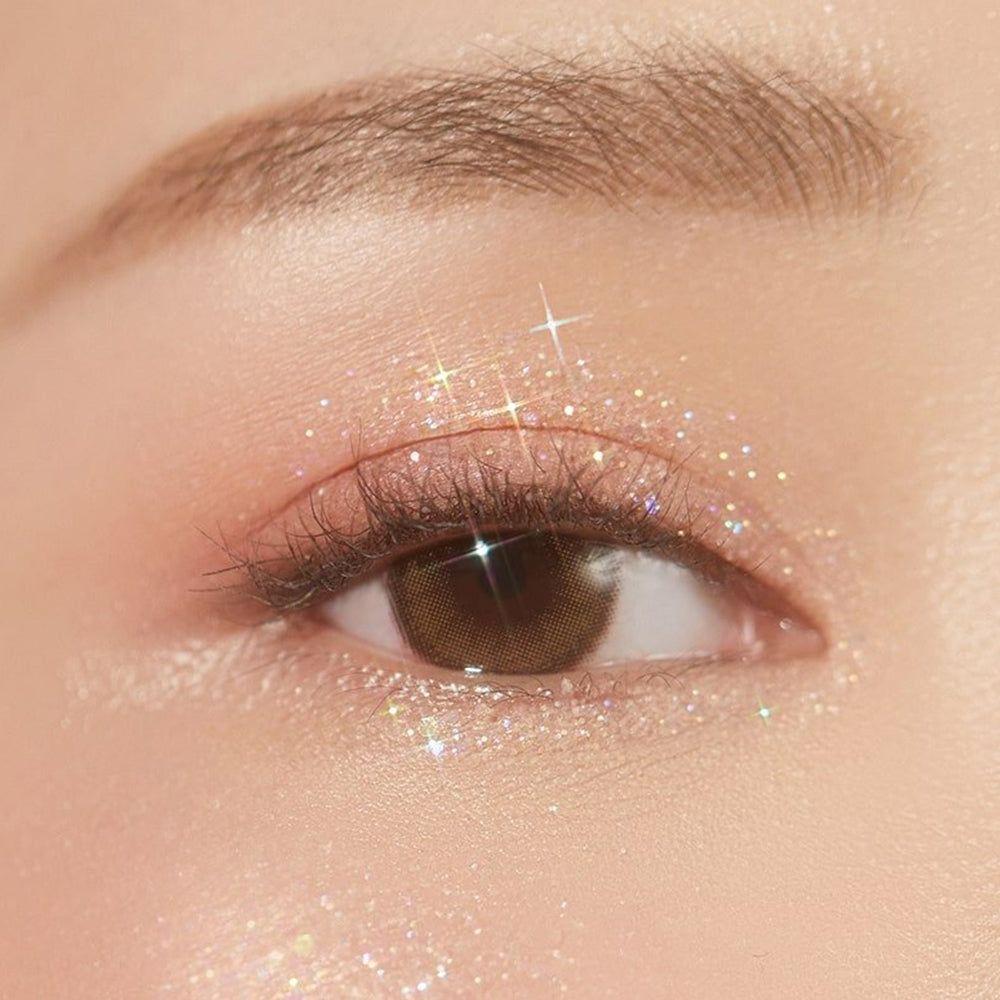 Nahaufnahme eines Auges mit schimmerndem Lidschatten und Glitzerpartikeln.