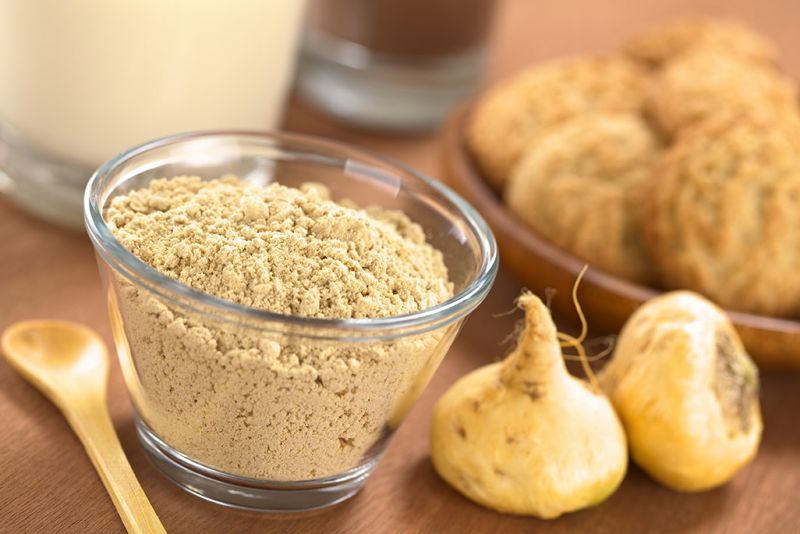 Glas mit Maca Pulver, daneben Wurzeln und Kekse. Holz-Löffel.