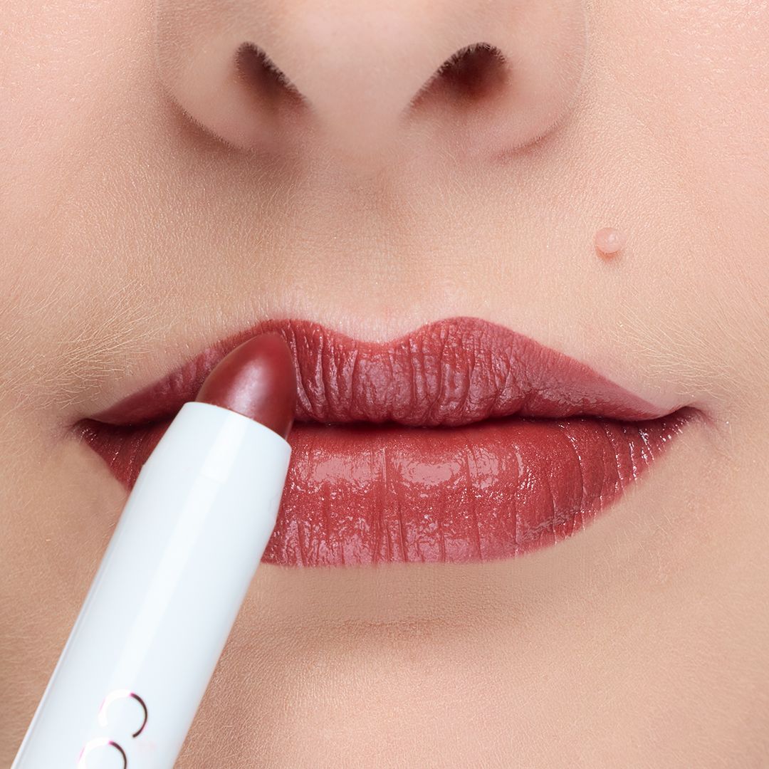 Lippenstift in Stiftform, Farbe Rotbraun, wird auf Lippen aufgetragen. Weißer Stift mit Logo.