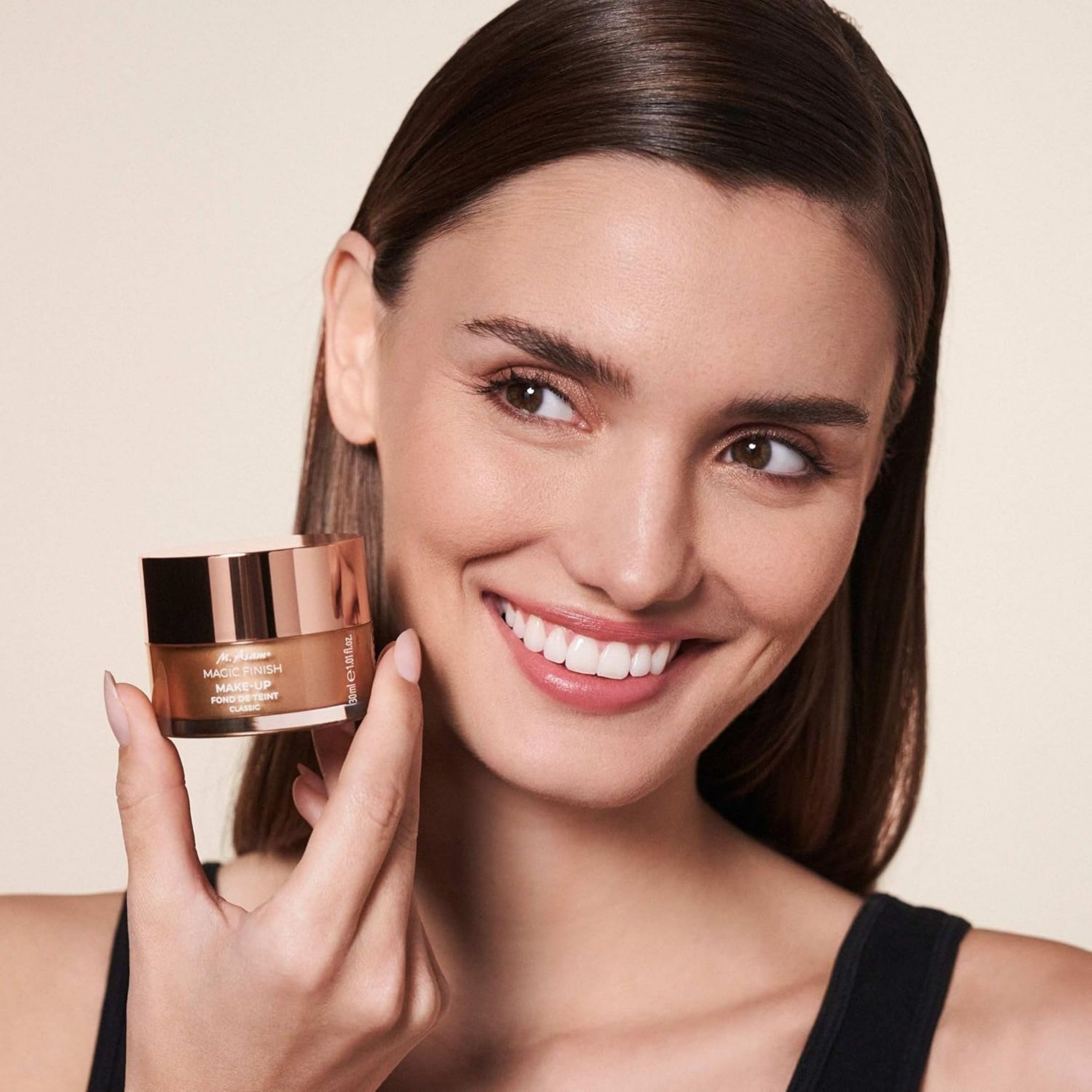 Donna che tiene il fondotinta mousse M. Asam Magic Finish. Sorride.