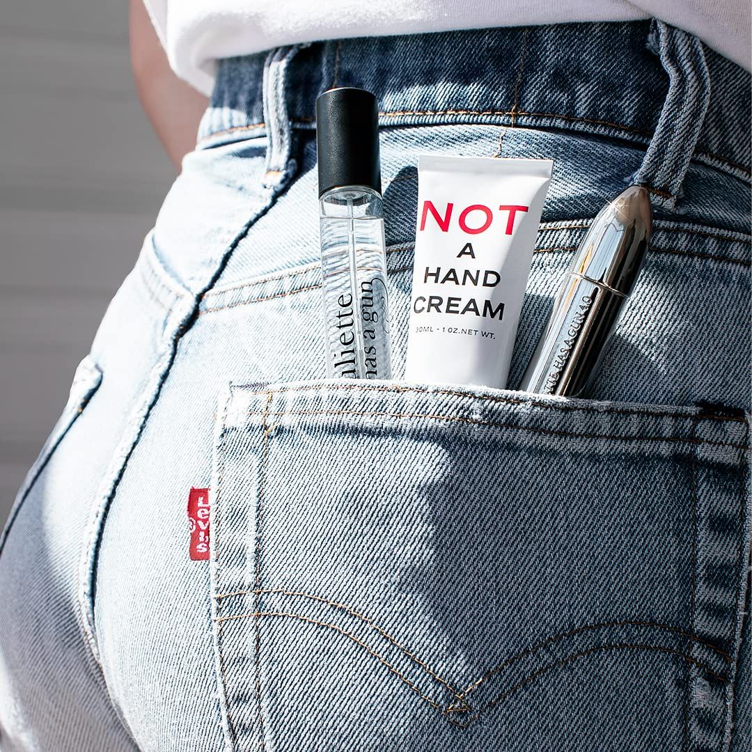 Handcreme-Tube 'NOT A HAND CREAM' in Jeans-Gesäßtasche. Daneben Parfümflakon und Zerstäuber. Marke: Juliette Has a Gun.