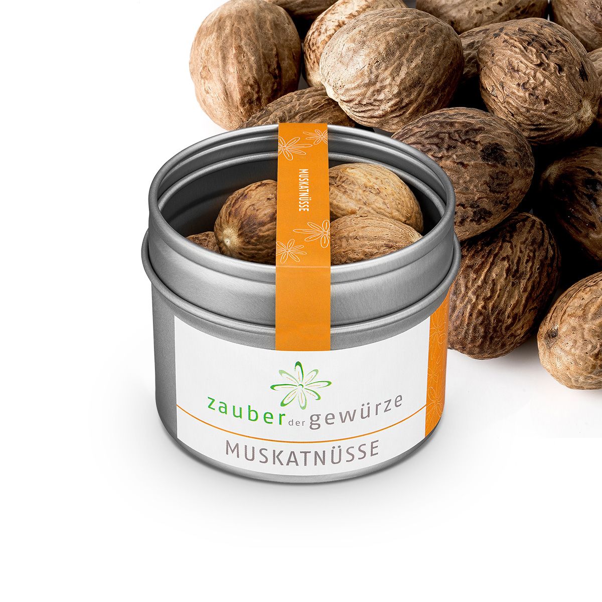 Metallbehälter mit Muskatnüssen. Orangefarbener Aufkleber mit Text. Aufschrift: Zauber der Gewürze Muskatnüsse. Viele Muskatnüsse drumherum.