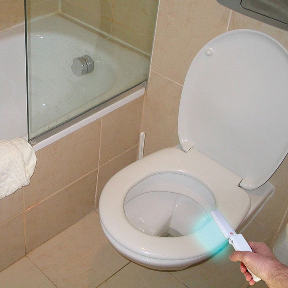 Hand gehaltenes, weißes UV-C-Desinfektionslicht in einem Badezimmer. Licht scheint in eine Toilette.