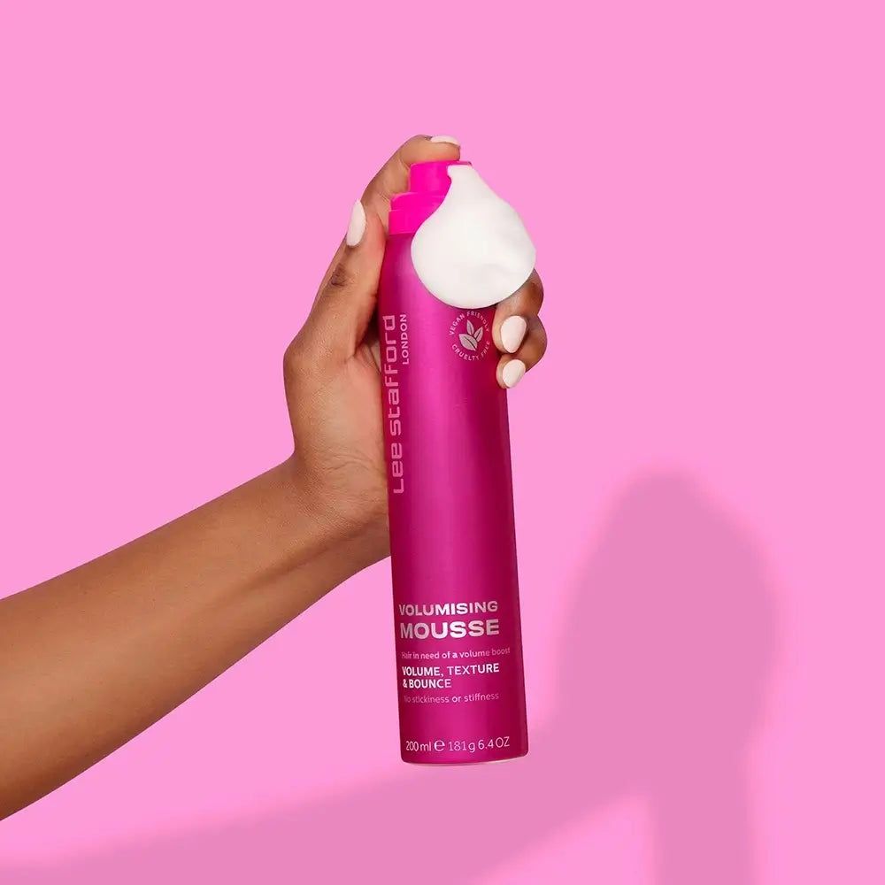 Hand hält eine pinke Dose Lee Stafford Volumising Mousse, aus der weiße Mousse austritt.