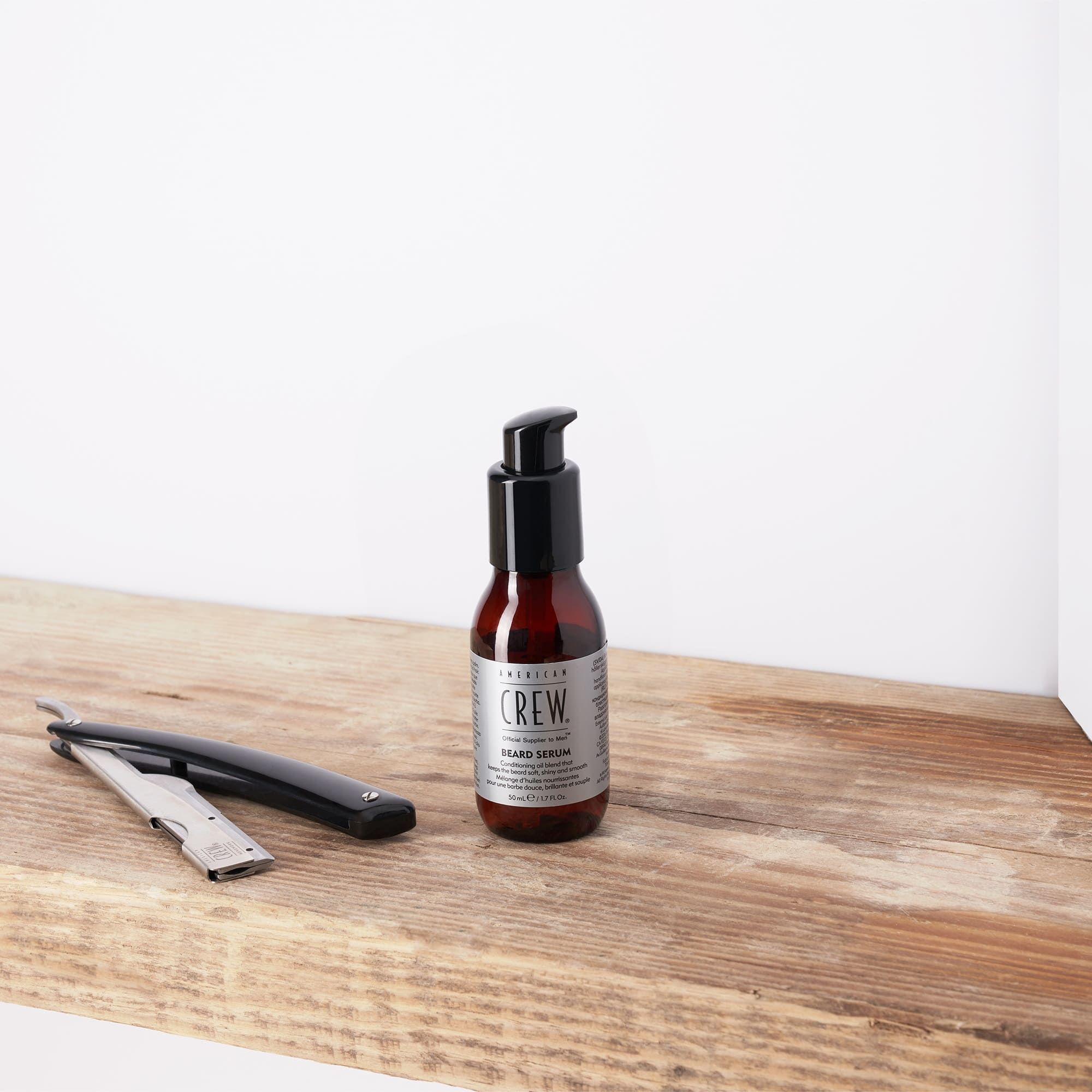 AMERICAN CREW Bartserum Flasche und Rasiermesser auf Holzregal.
