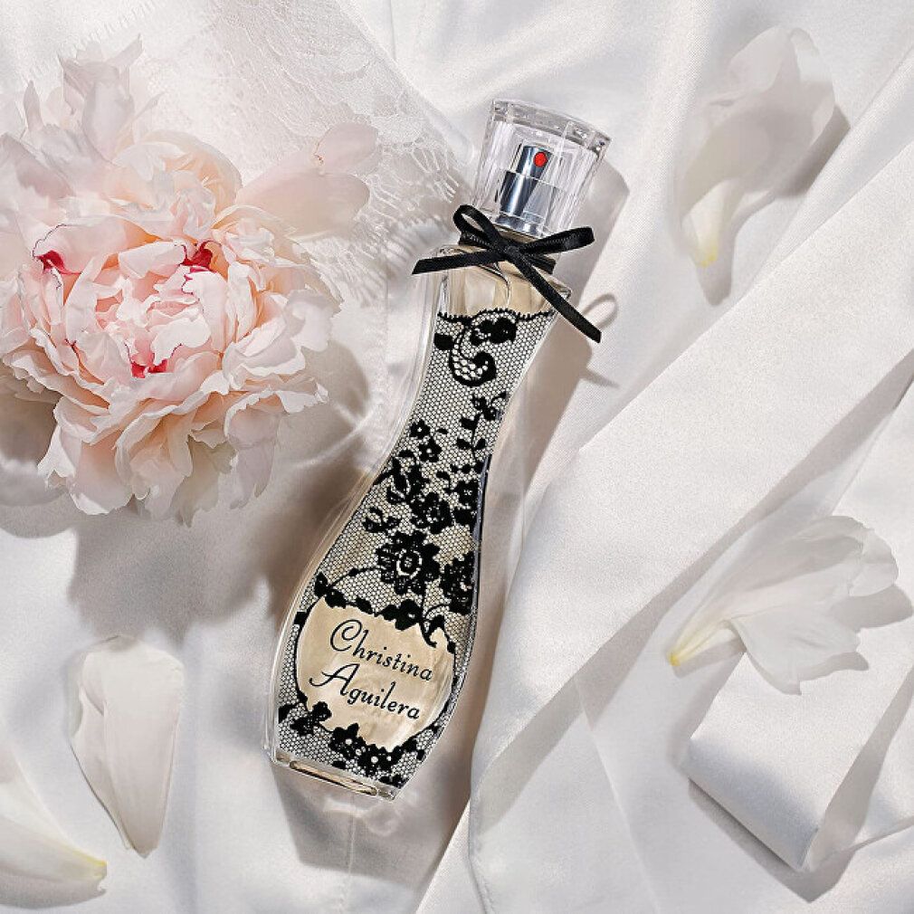 Christina Aguilera Eau de Parfum Flakon auf weißem Stoff mit Pfingstrose.