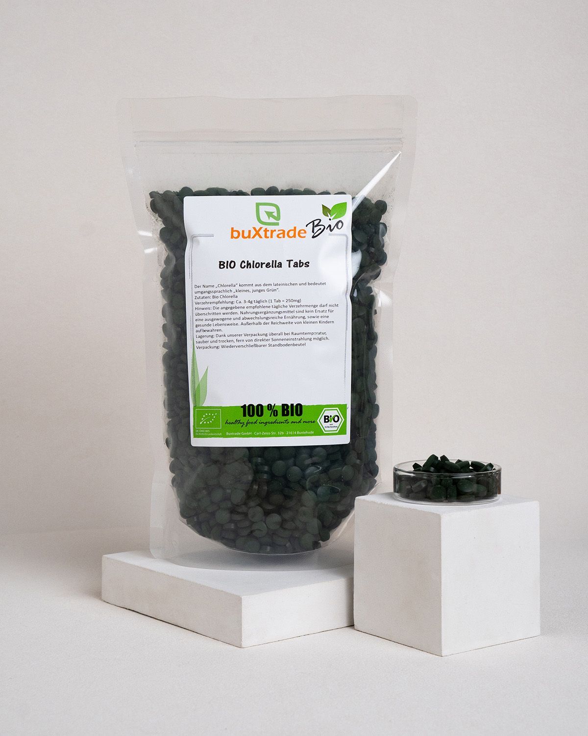 Transparente Tüte mit grünen Tabletten und eine kleine Glasschale mit Tabletten. Auf der Verpackung steht 'buXtrade Bio'.