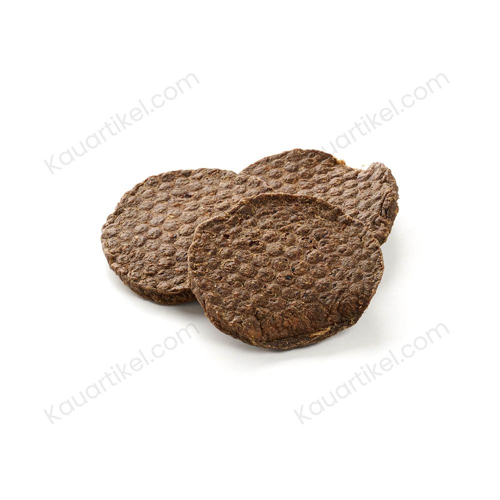 Ein Hund hält einen runden Rinder-Snack im Maul, weitere Snacks liegen auf einem Baumstumpf.