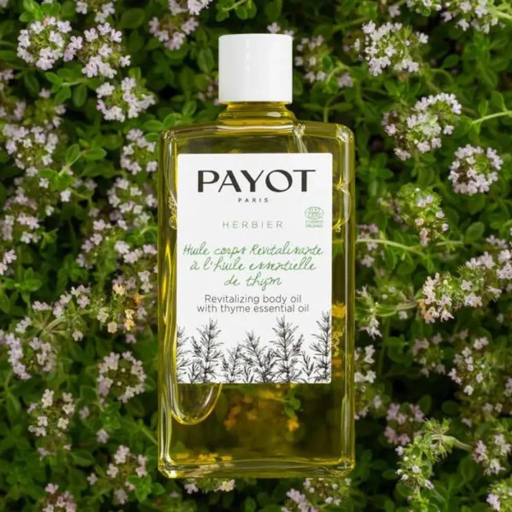 PAYOT Revitalisierende Körperöl mit Thymianöl in klarer Flasche, umgeben von Kräutern.
