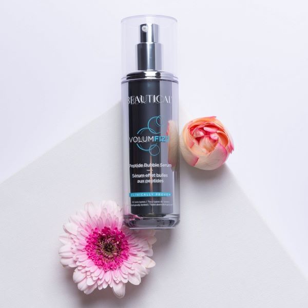 Beautical Volumfizz Peptidbubbleserum. Silberne Flasche mit Sprühkopf. Produktname und Details auf dem Etikett. Mit Blumen.