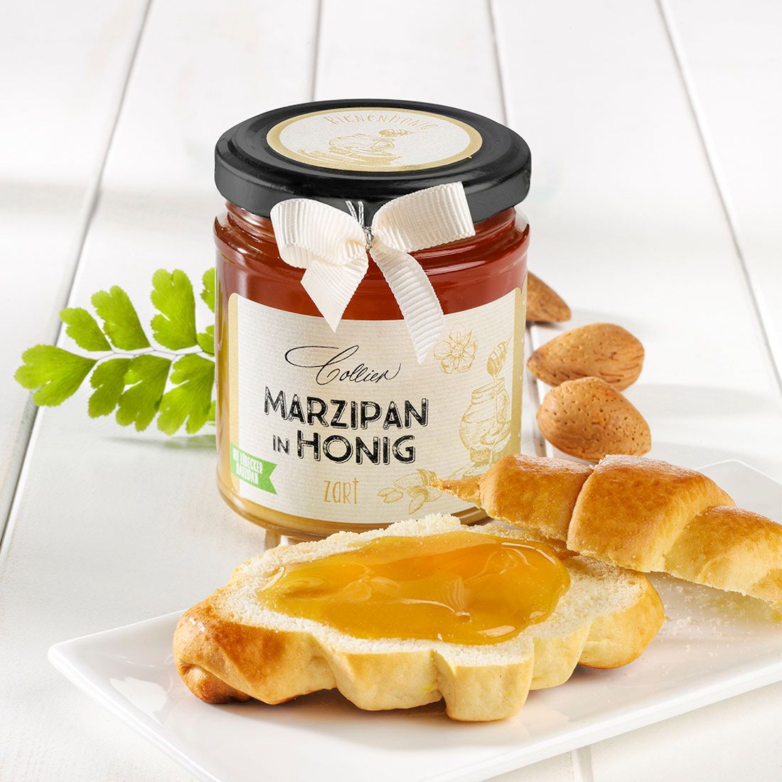 Glas Marzipan in Honig, Etikett, schwarzer Deckel, Schleife. Schriftzug: Marzipan in Honig. Zart. Brot mit Honig, Mandeln, Blatt.