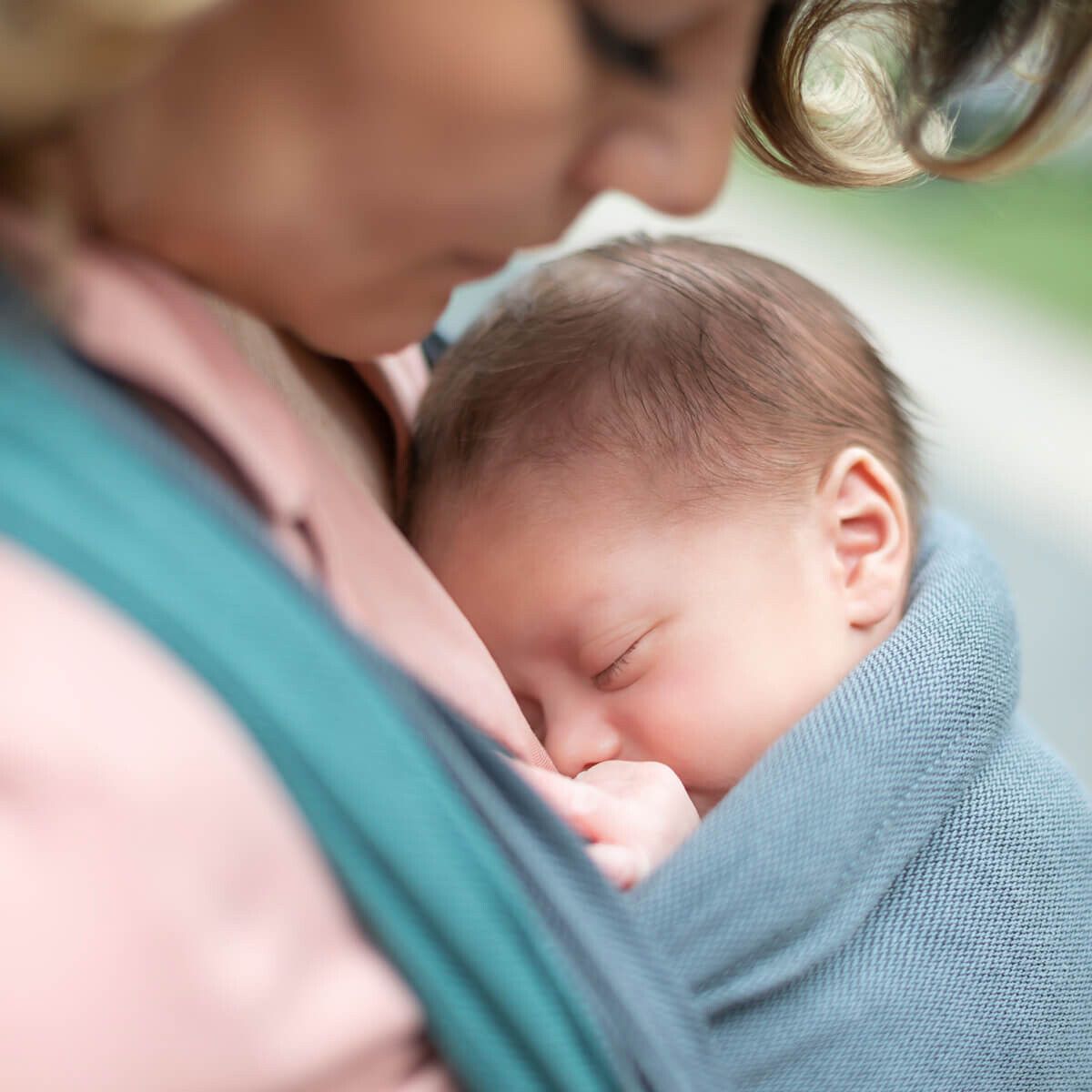 Baby in blauer Trage, schlafend. Frau hält Baby. Nahaufnahme.