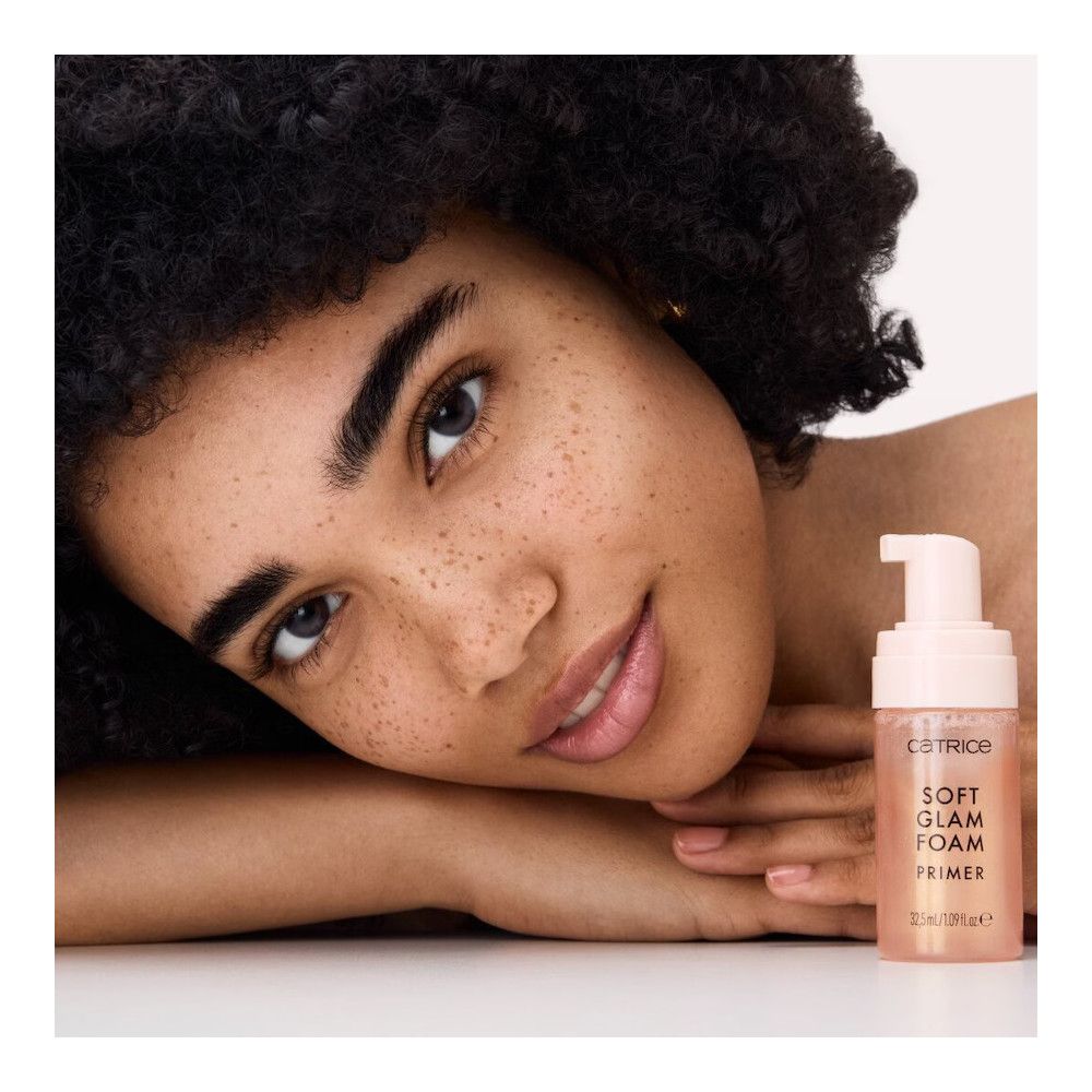 Frau mit Locken und Foundation-Flasche. Aufschrift: Catrice, Soft Glam Foam Primer, 32,5 ml/1.09 fl.oz.e.