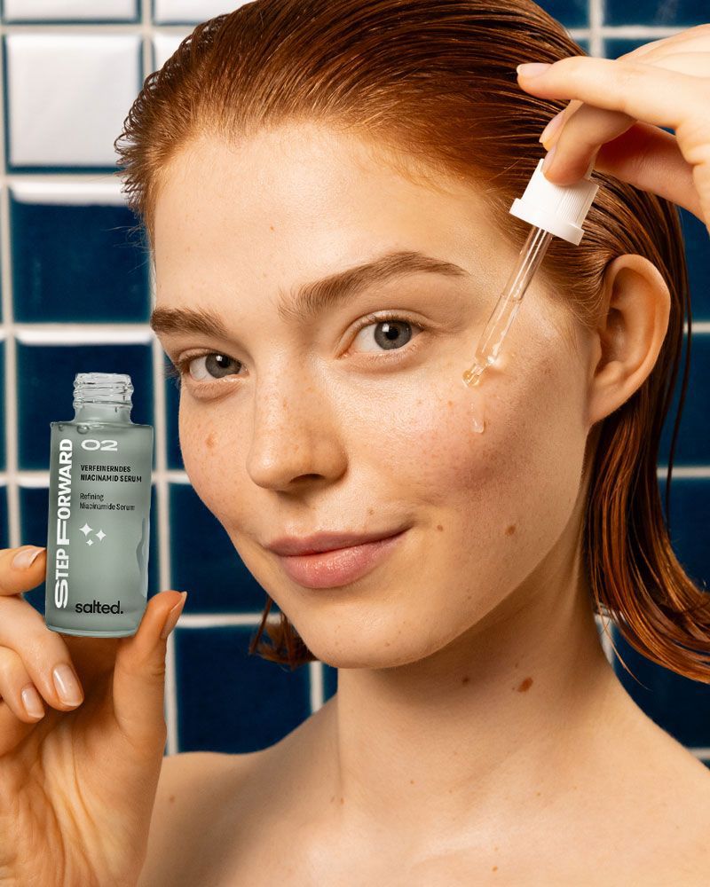 Frau hält Flasche mit Pipette. Aufschrift: Verfeinerndes Niacinamid Serum, salted. Pipette tropft.