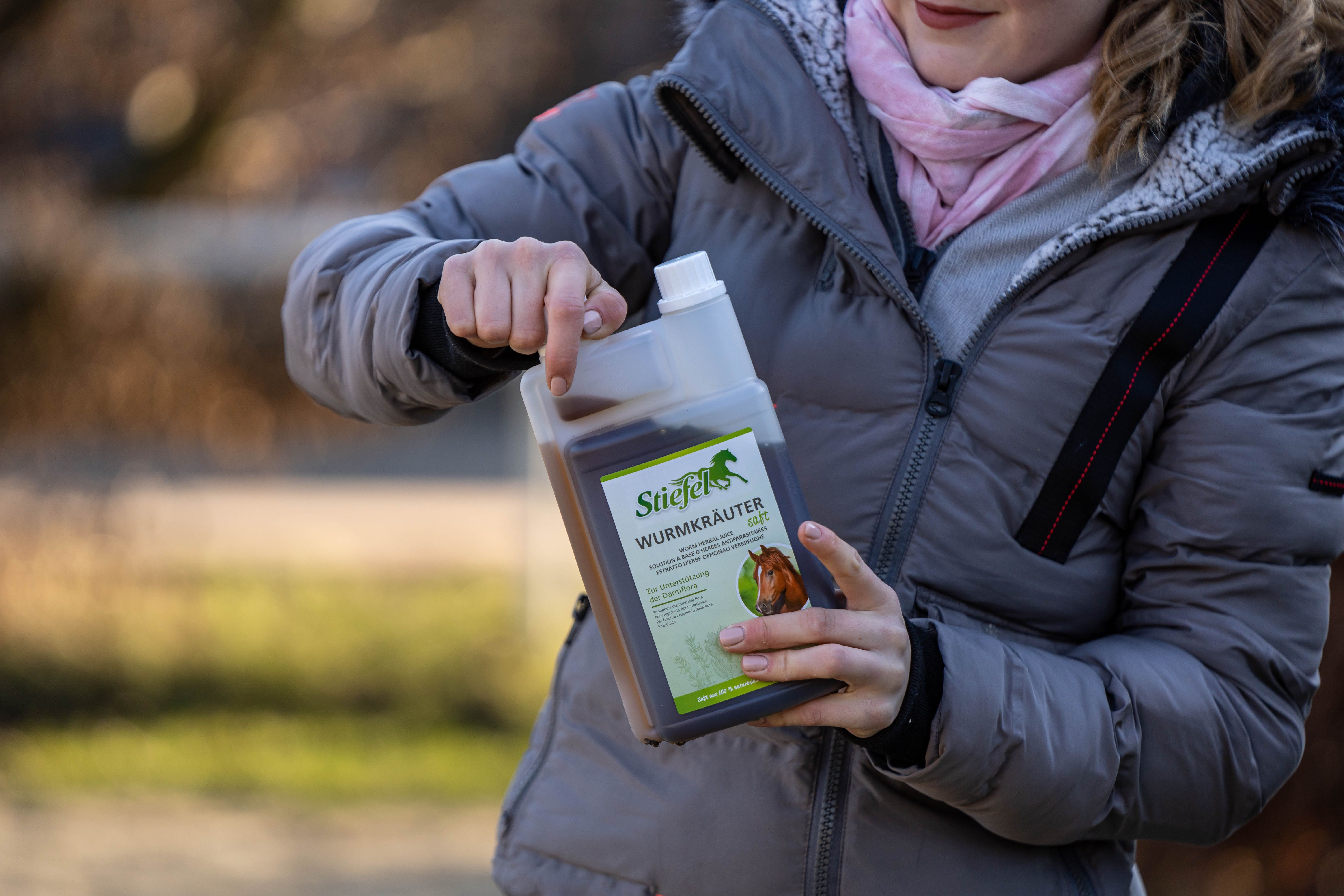 Person hält eine Doppelkammerflasche mit brauner Flüssigkeit. Aufschrift: Stiefel Wurmkräuter. Die Flasche wird geöffnet.