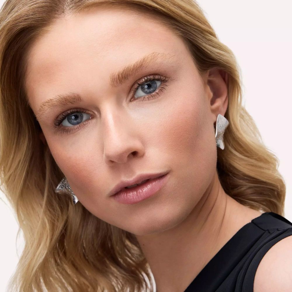 Porträt einer Frau mit blonden Haaren und blauen Augen. Sie trägt silberne Ohrringe.