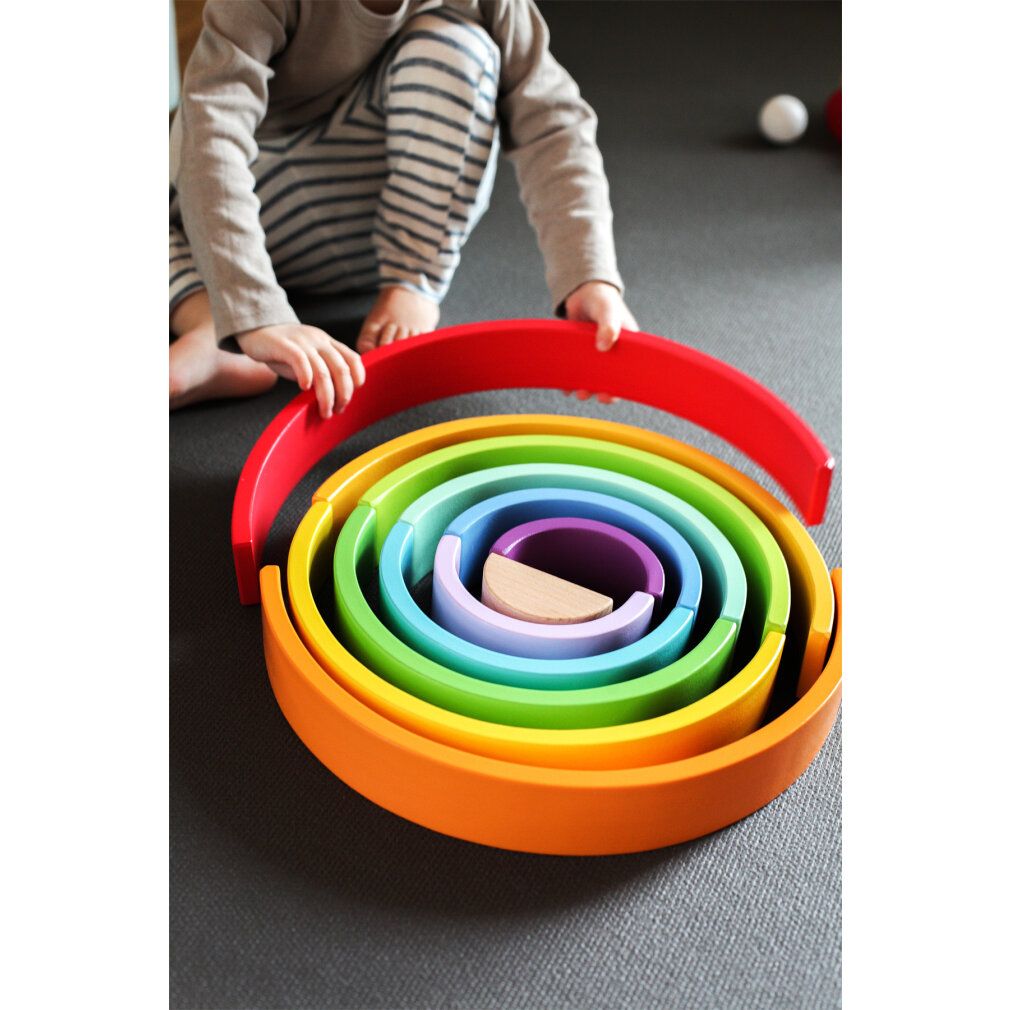 Kind spielt mit Regenbogen-Holzbausteinen. Holzbausteine in Regenbogenfarben, verschiedene Größen. Kugel.