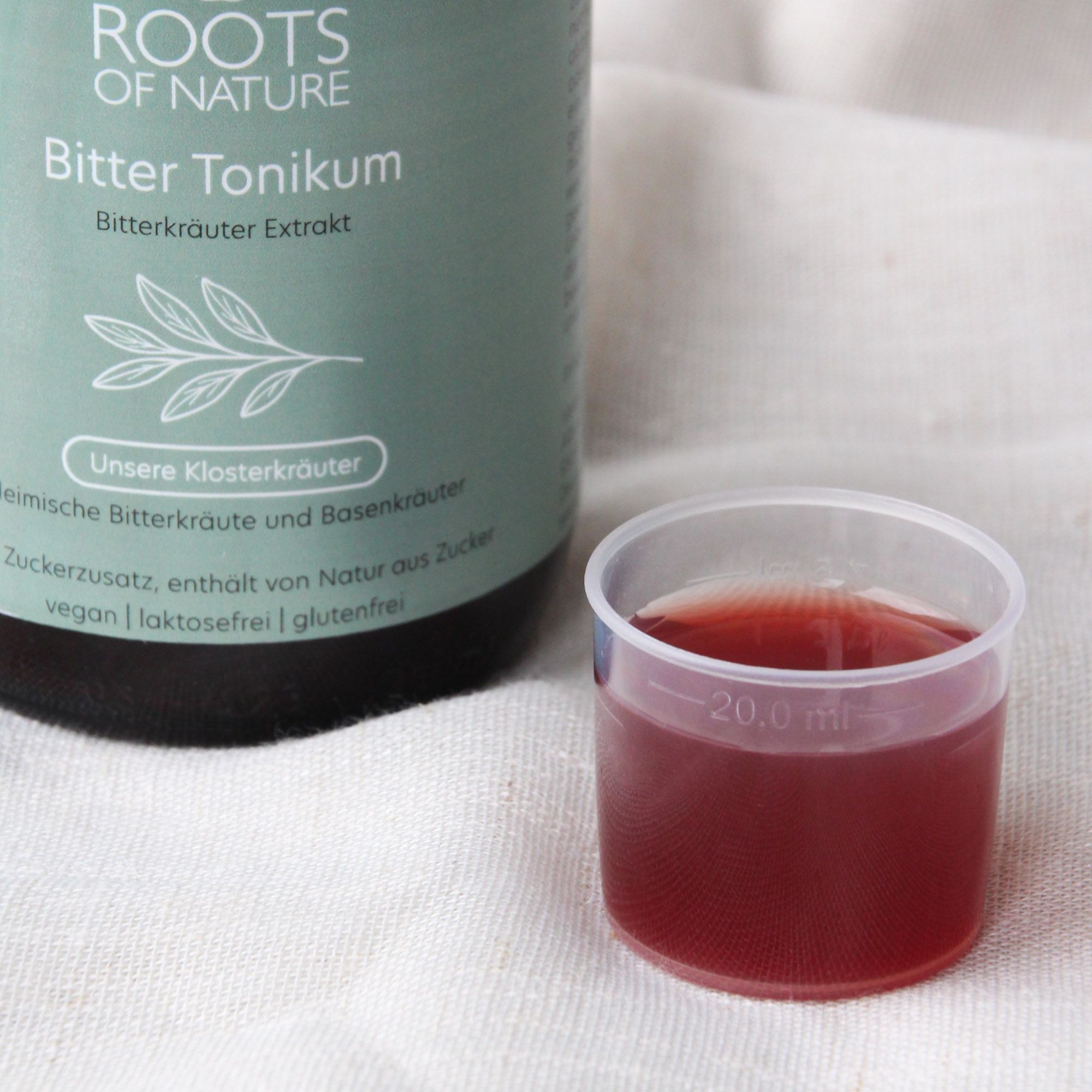 Braune Flüssigkeit in einer Flasche und Messbecher. Aufschrift: Bitter Tonikum. Vegan, laktosefrei, glutenfrei.