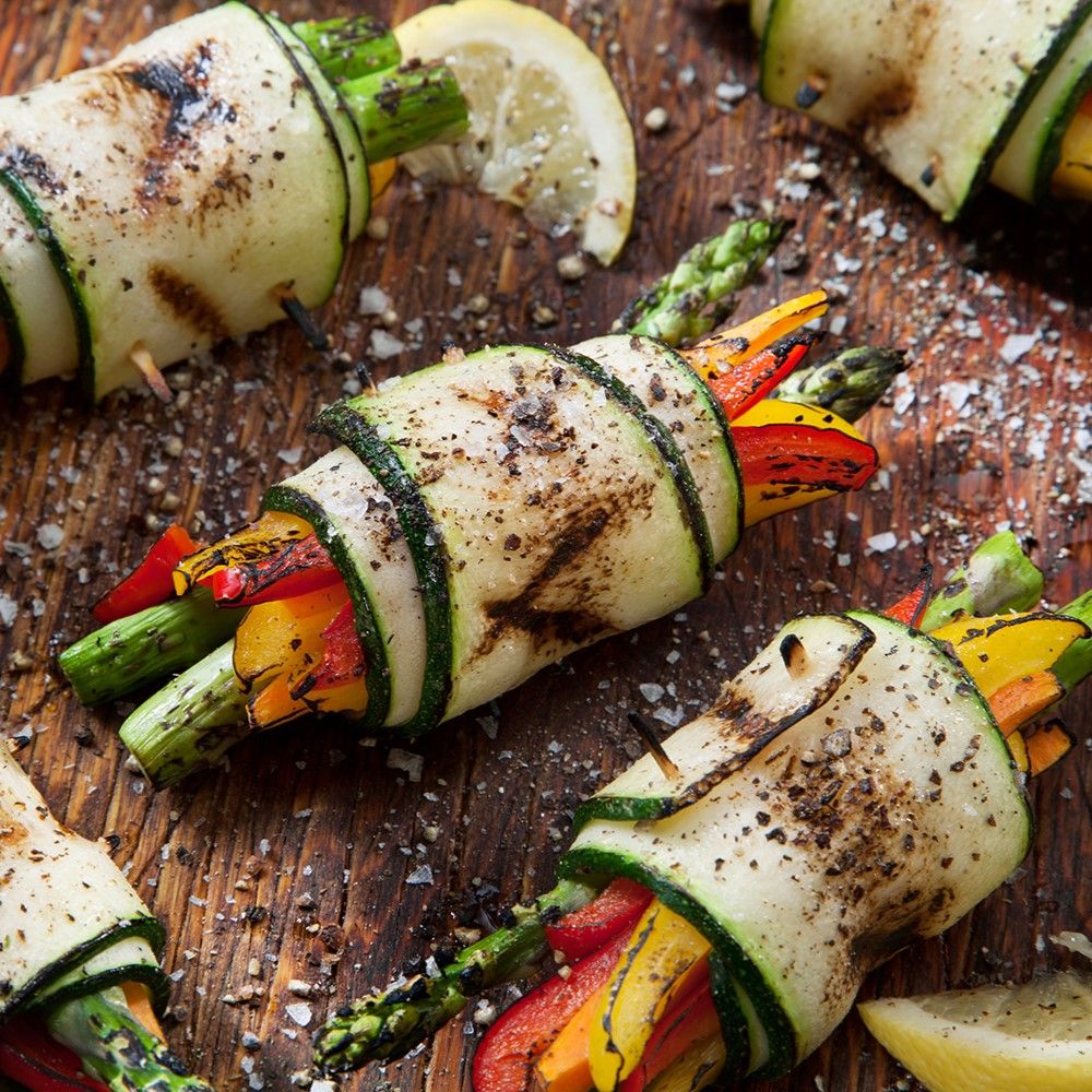 Gerollte Zucchinischeiben mit Gemüsefüllung. Auf Holzbrett. Spargel, Paprika und Zitrone sichtbar.