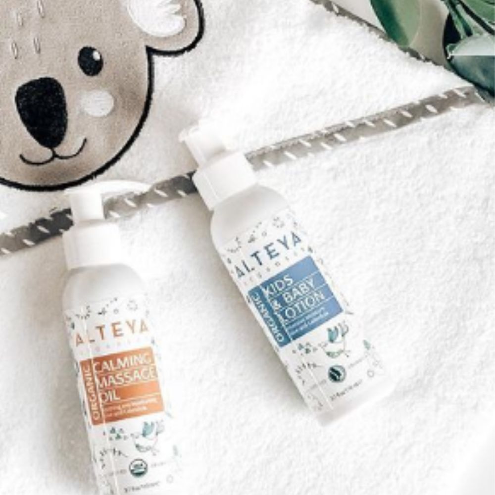 Zwei Flaschen mit Pumpen. Aufschrift: Alteya Organics. Eine Flasche: Kids & Baby Lotion. Die andere: Calming Massage Oil. Auf einem Handtuch.