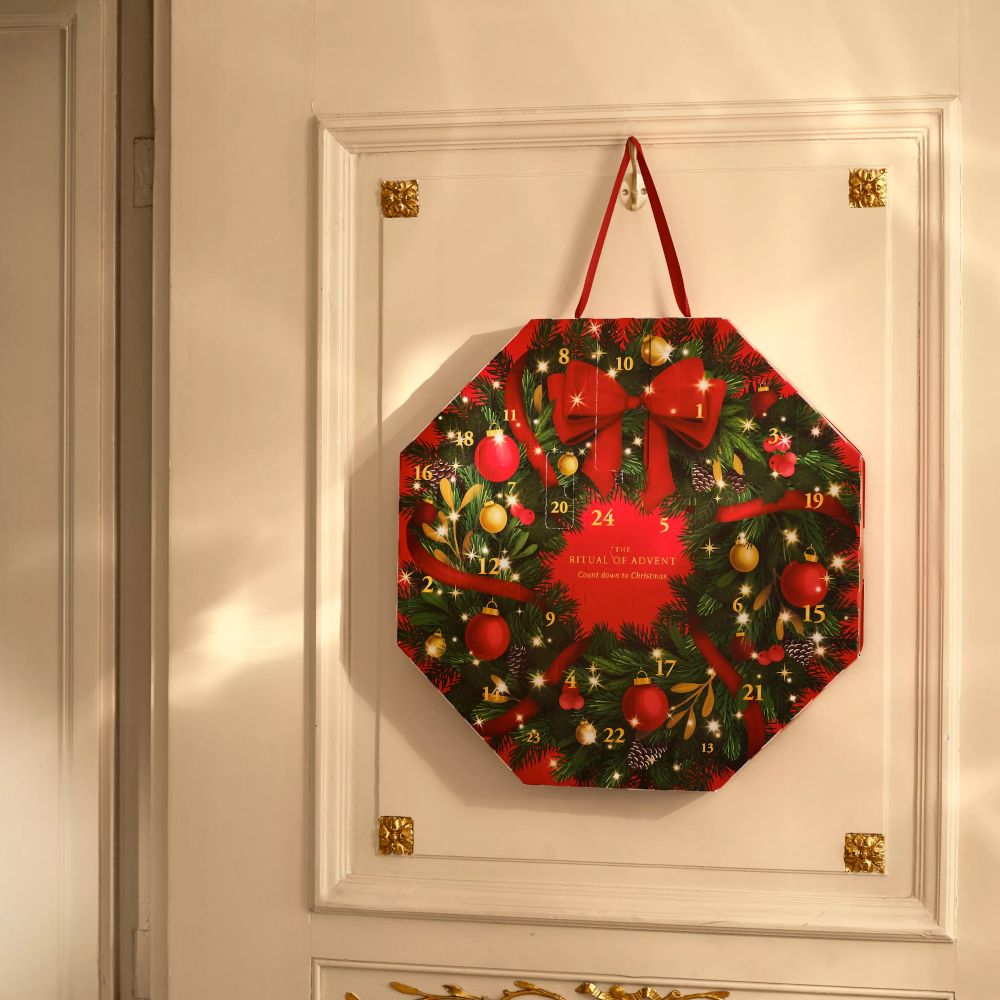 Achteckiger Adventskalender mit weihnachtlichem Design, an einer Tür hängend. Rote Schleife, Kugeln und Tannenzweige.