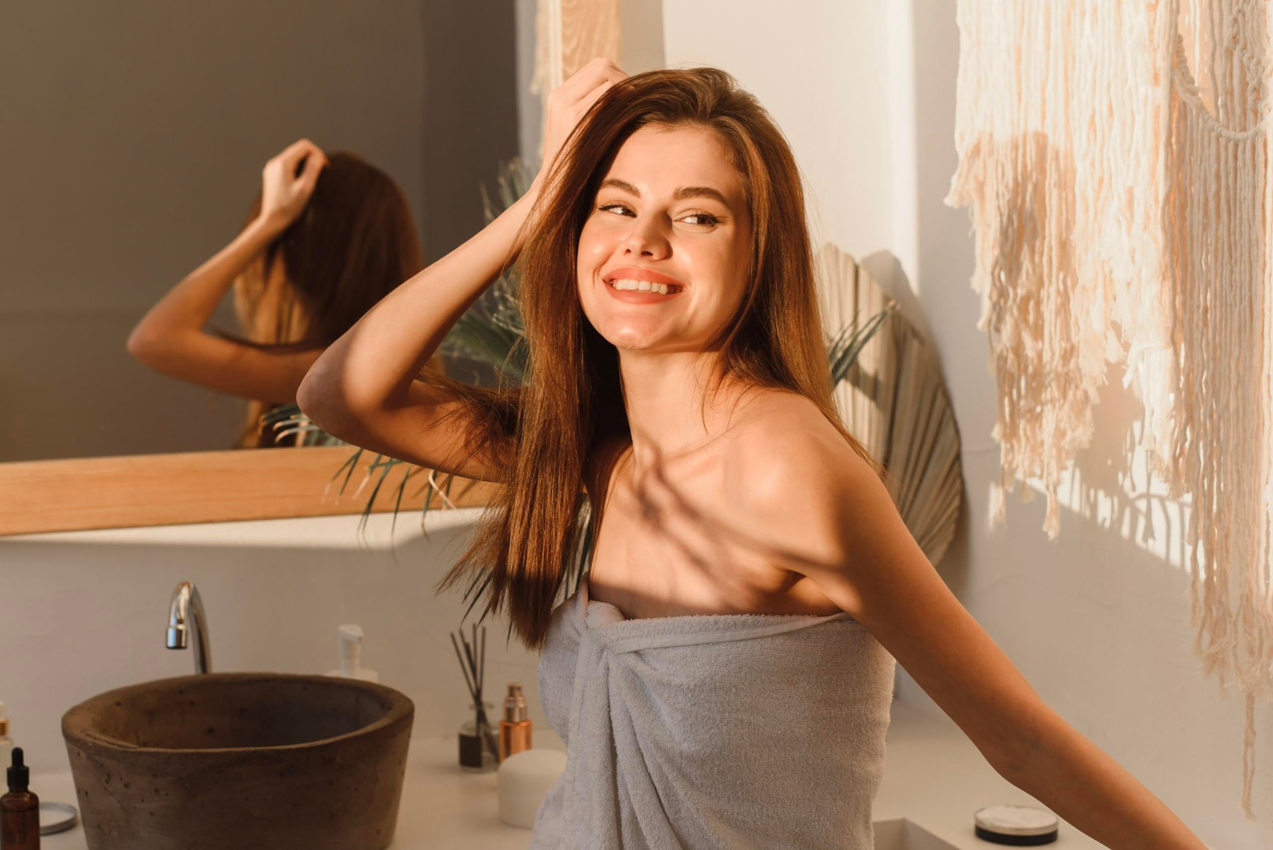 Frau im Badezimmer, in ein Handtuch gewickelt. Spiegel und Waschbecken im Hintergrund.