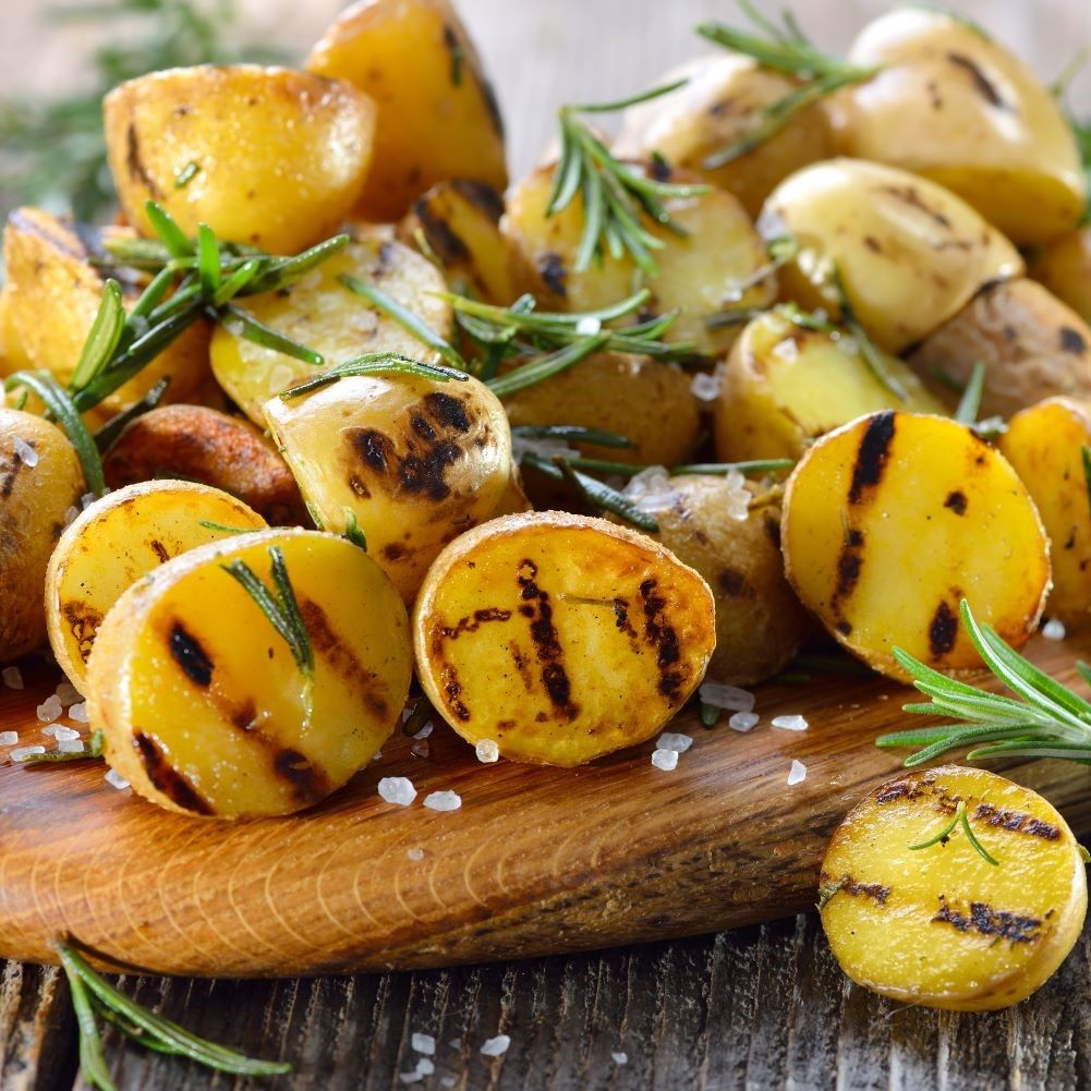 Gegrillte Kartoffeln mit Rosmarin auf einem Holzbrett. Einige Salzkristalle sind sichtbar.