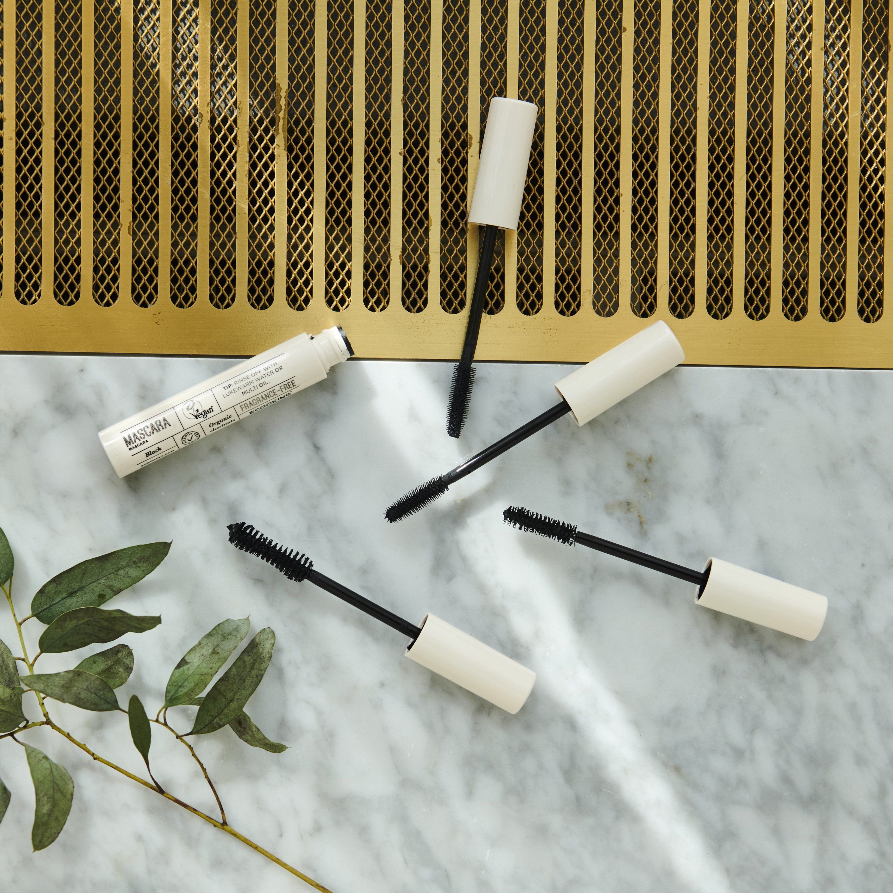 Mehrere Mascara-Tuben mit geöffneten Bürsten auf einer Marmoroberfläche. Weiße Deckel, schwarze Bürsten. Vegan-Logo sichtbar.