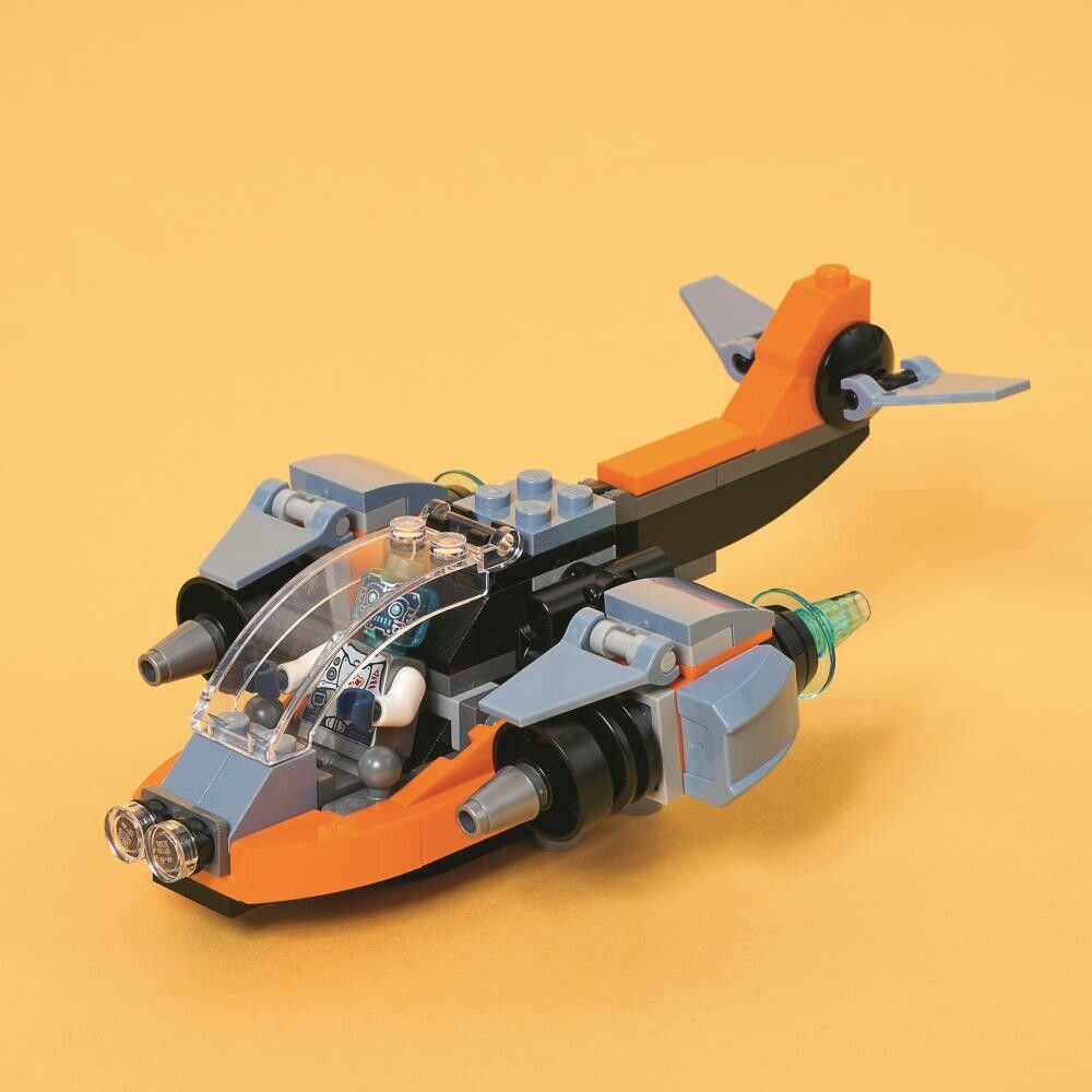 Il modello LEGO Creator Cyber-Drone è posto su uno sfondo giallo. Il modello è arancione, grigio e blu con elementi trasparenti. Ha un abitacolo e ali. Il modello è visibile in dettaglio.