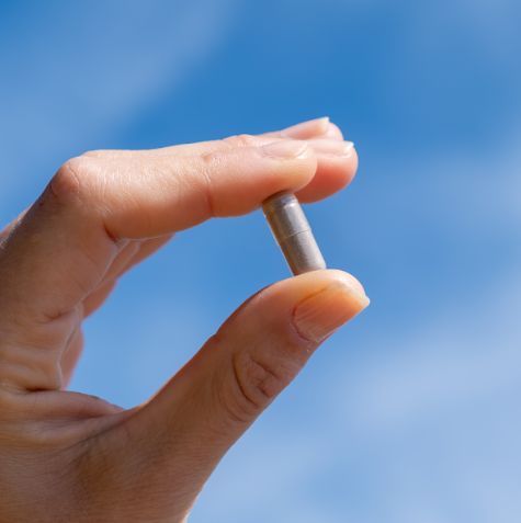 Hand hält eine einzelne Aavalabs Eisenbisglycinat Kapsel vor blauem Himmel.